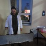 Uśmiechnięty mężczyzna w czapce stoi koło grilla